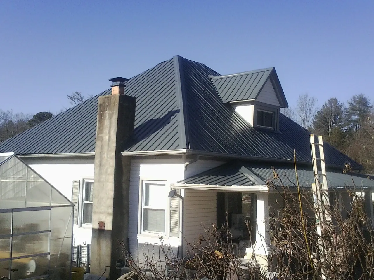 Dark blue standing seam metal roof on a white farmhouse with dormer — Slate & Tile Roof Repair by Roofing Brothers in Cherry Tree