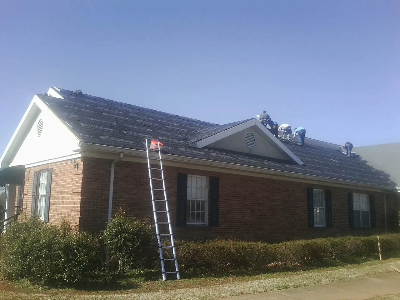 Crew tearing shingles off a brick ranch roof with a ladder set — Emergency Roof Repair work by our crew in Cherry Tree