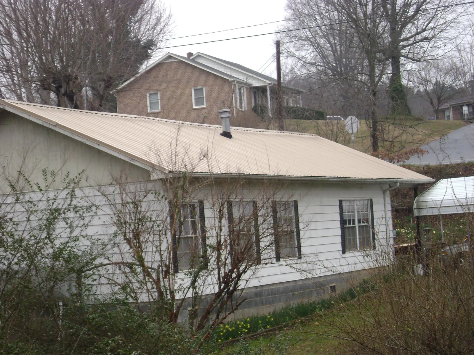 Tan metal roof on a white sided house set into a hillside — Commercial Roofing by Roofing Brothers in Cherry Tree